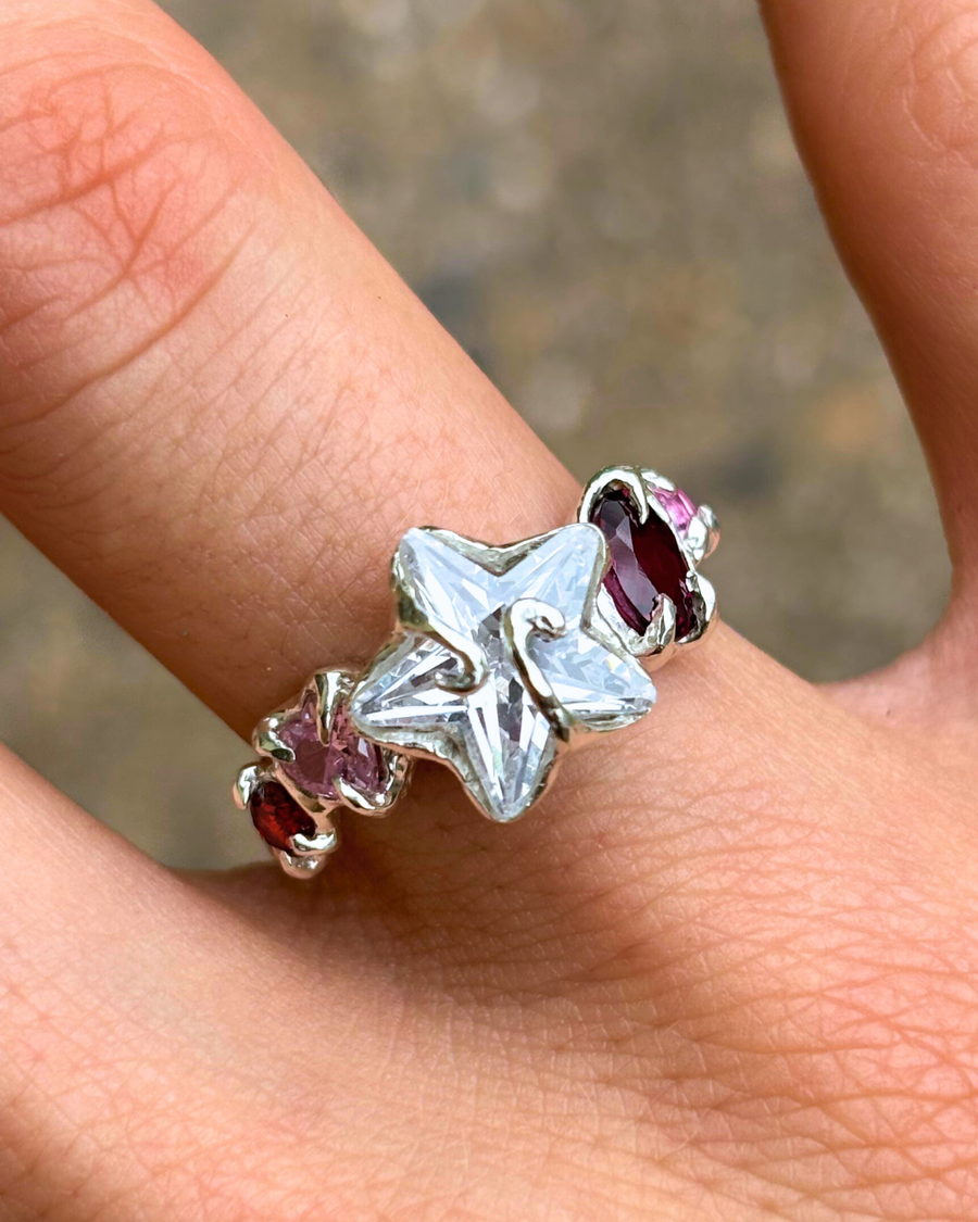 Silver star-shaped ring with pink gemstones on a finger against a blurred background