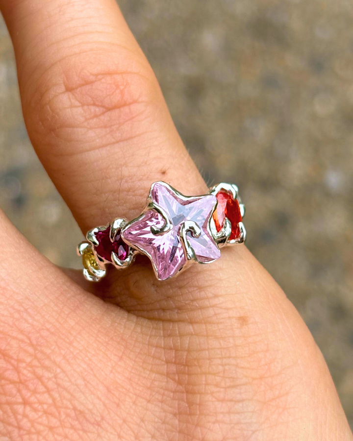 Star-shaped ring with pink gemstone on a finger against a blurred background